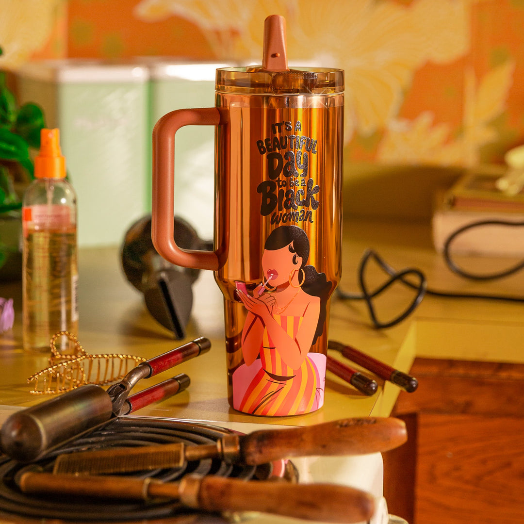 Copper Luxe HydraLock tumbler with an illustrated Black woman applying pink lip gloss with a compact mirror, wearing gold hoops and a red, orange and yellow striped dress, beneath the black affirmation It's a Beautiful Day to Be a Black Woman